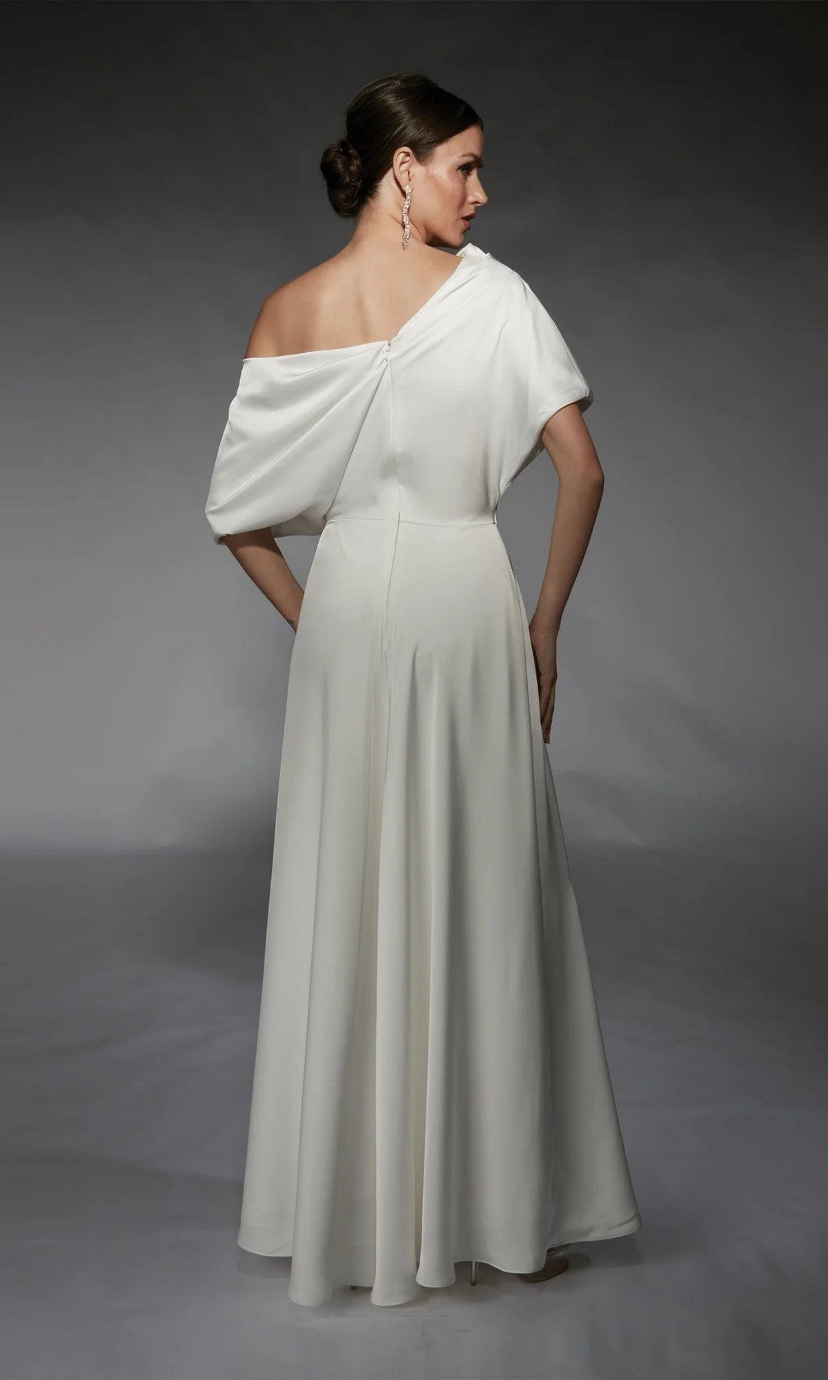 A woman wearing the Alyce 70072 Long White Jumpsuit, featuring an off-shoulder design and wide-leg pants, poses with her back to the camera against a gray background.